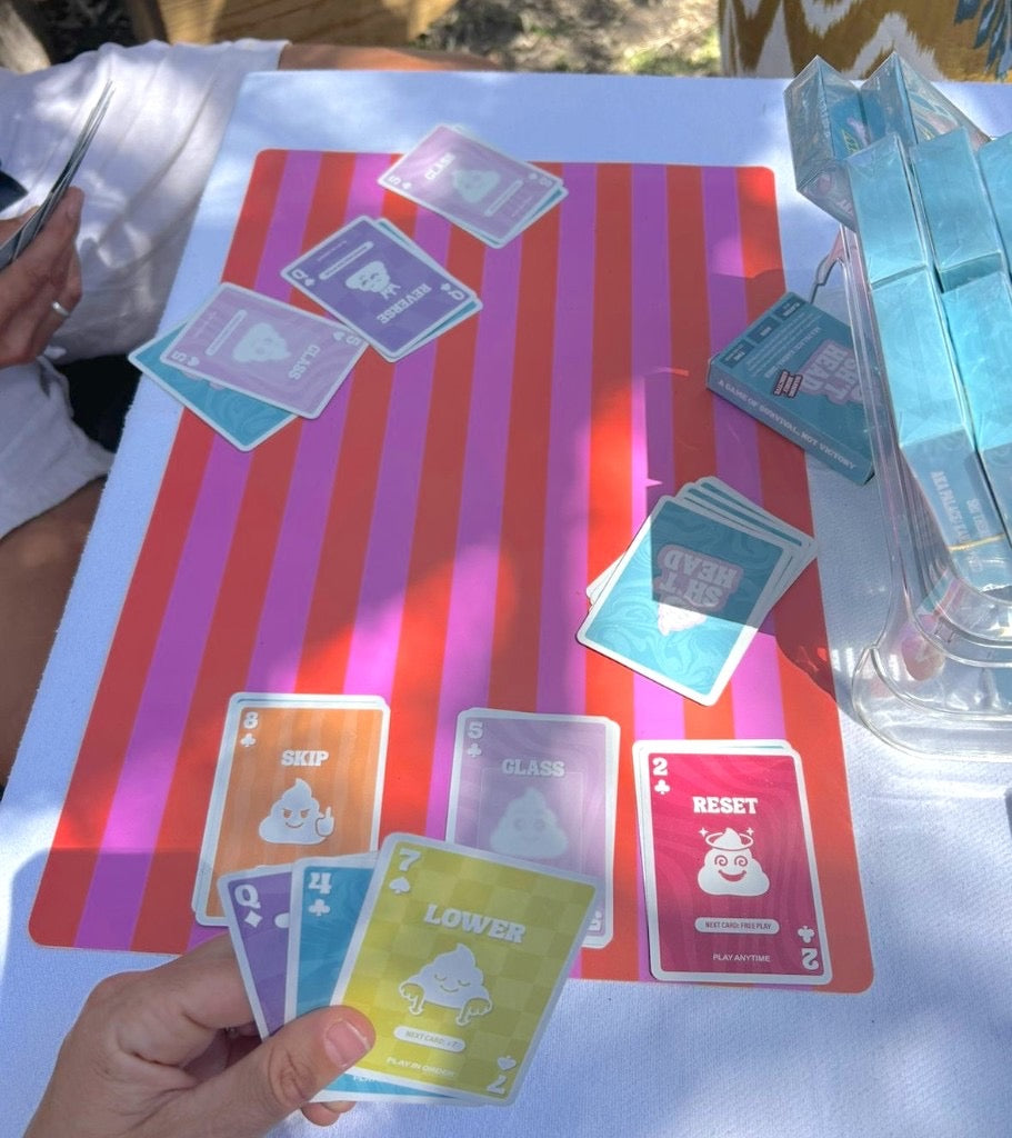 Sh*thead Card Game outdoor game in action — hands dealing cards on striped mat